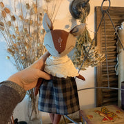Handmade linen fox spirit guardian doll with embroidered details, dressed in a dark plaid skirt and creamy muslin scarf, surrounded by dried herbs and natural botanical elements.